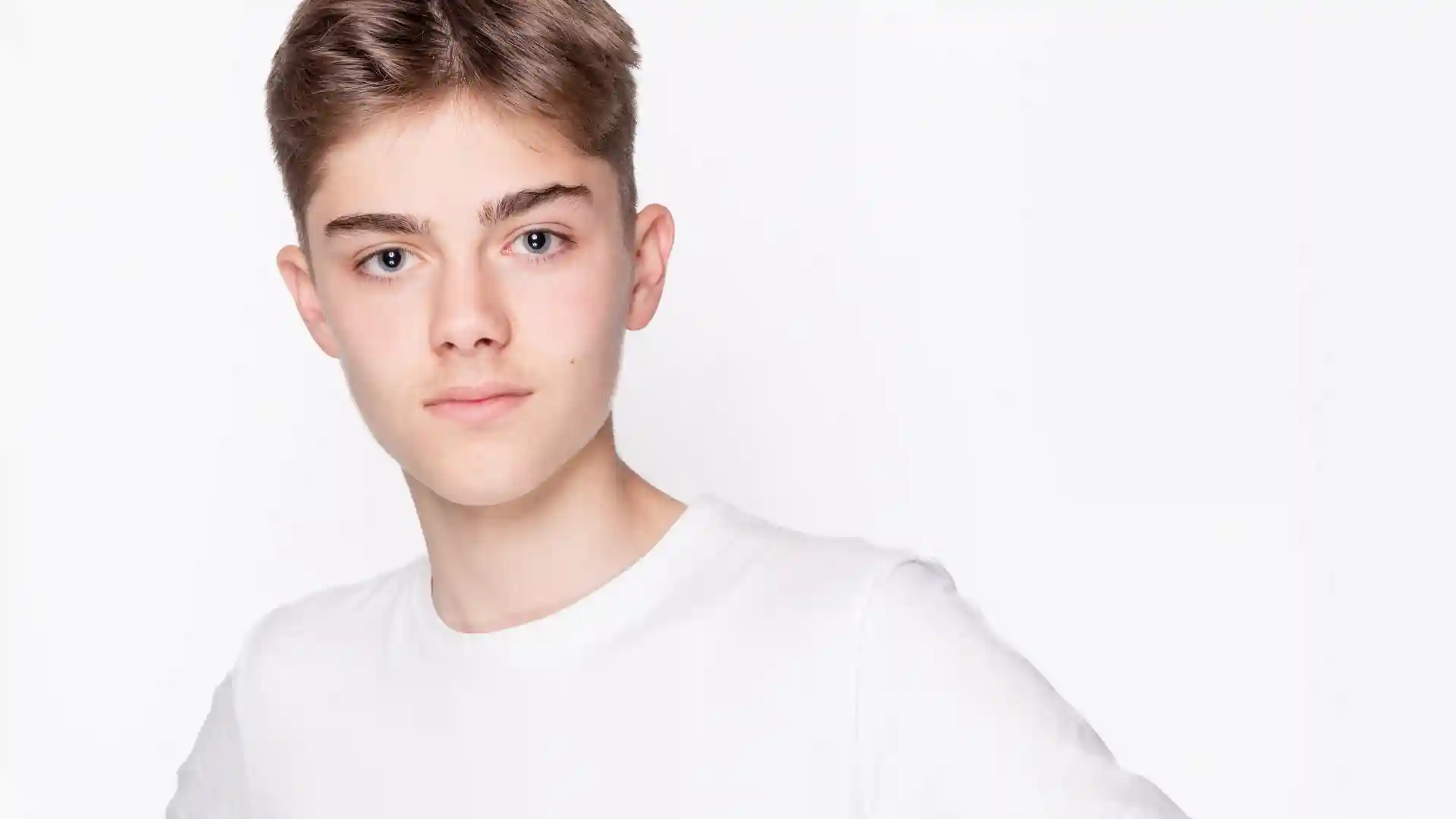 白い背景に白いTシャツを着た白人の青年がこちらを見ている