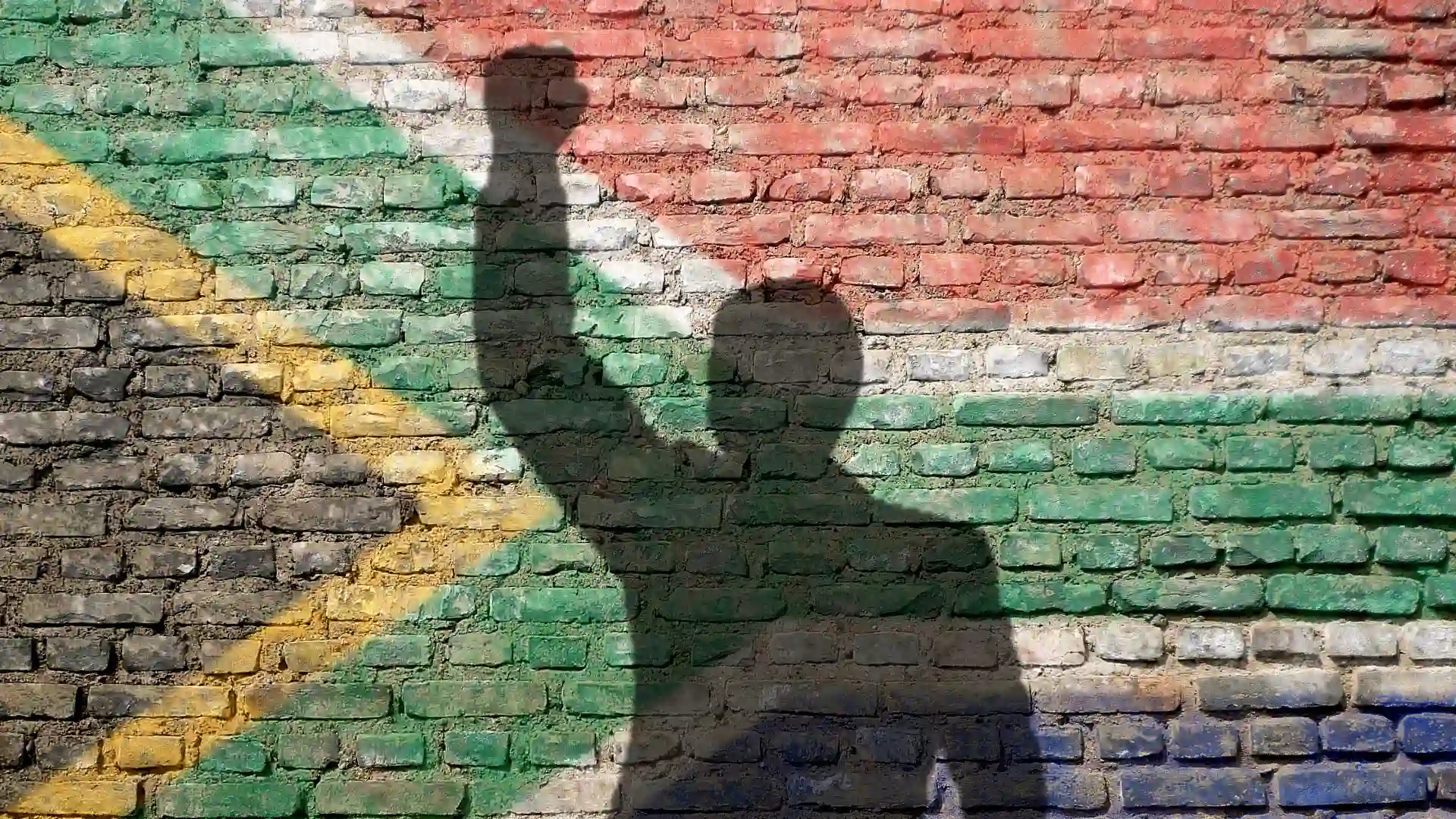 壁にアフリカ国旗の模様がスプレーされていて男の人が拳を振り上げている影が映っている