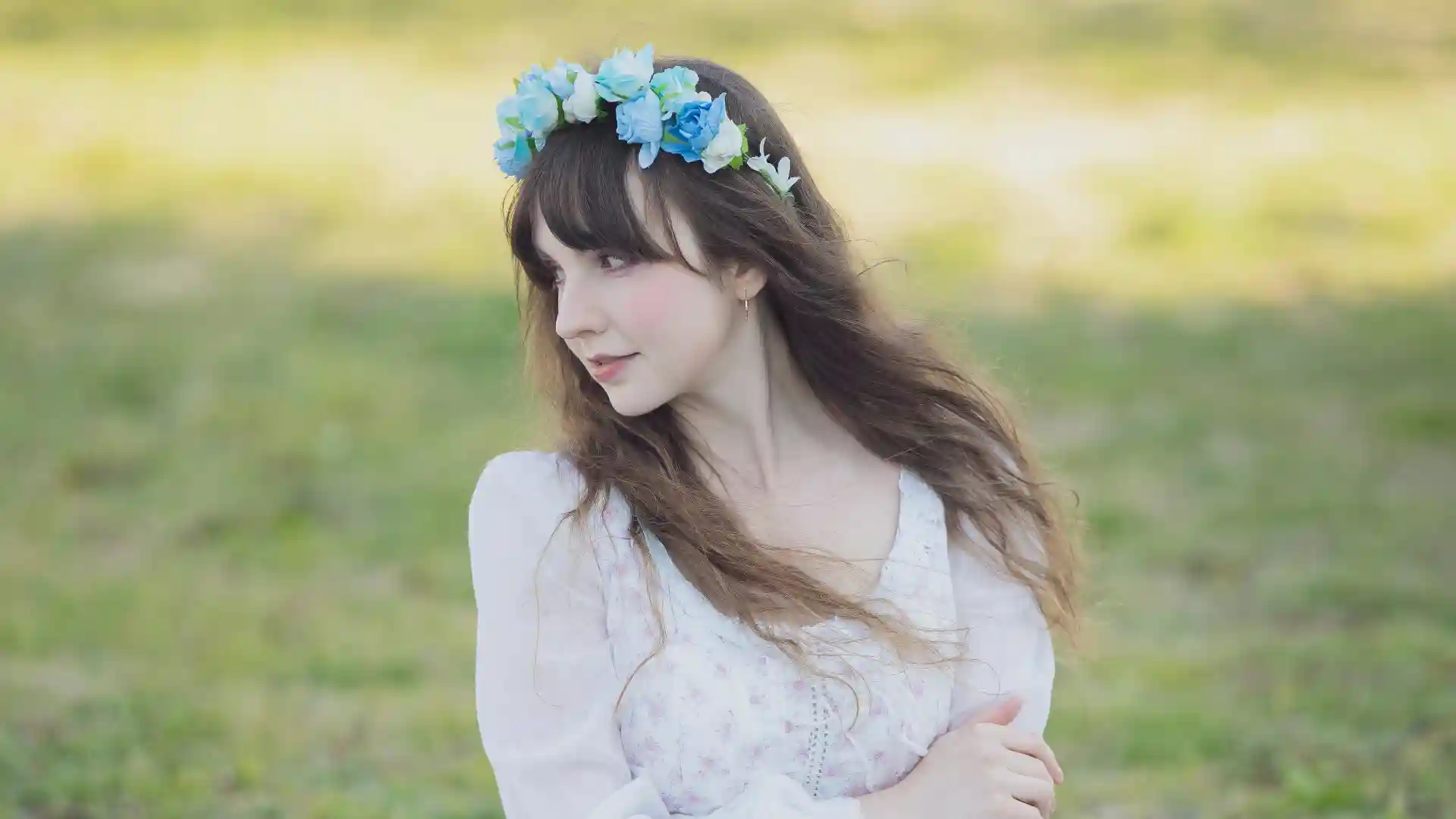 青い花冠を頭に乗せた女性がうつむいた状態で芝生の上に立っている