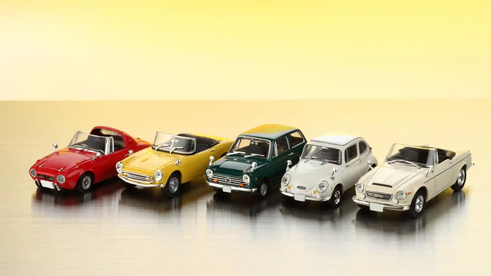 黄色い背景にクラシックなミニカーが5台横に並んでいる